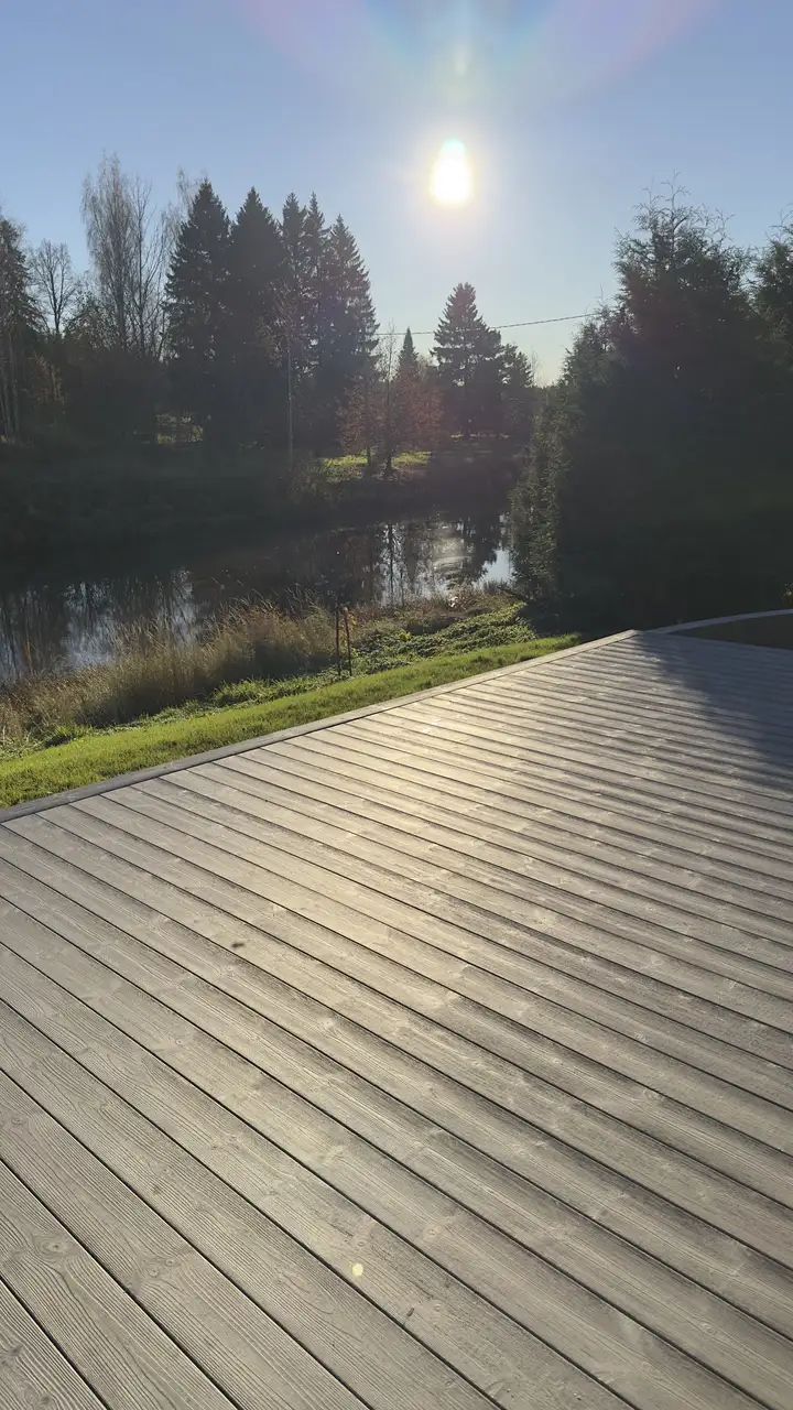 Matala aurinko paistaa terassin yli, taustalla joki ja puut.