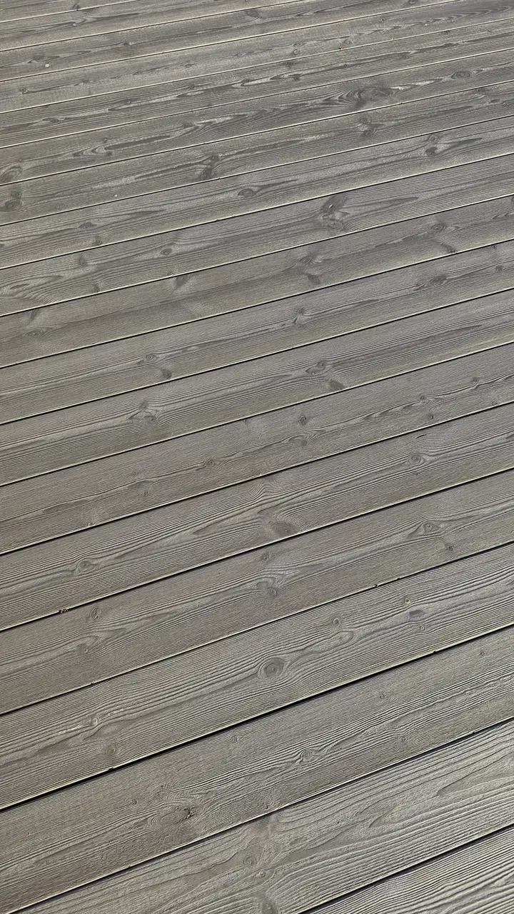 Lähikuva harjatusta harmaasta terassilaudasta, jonka vuosirenkaat erottuvat pinnassa.