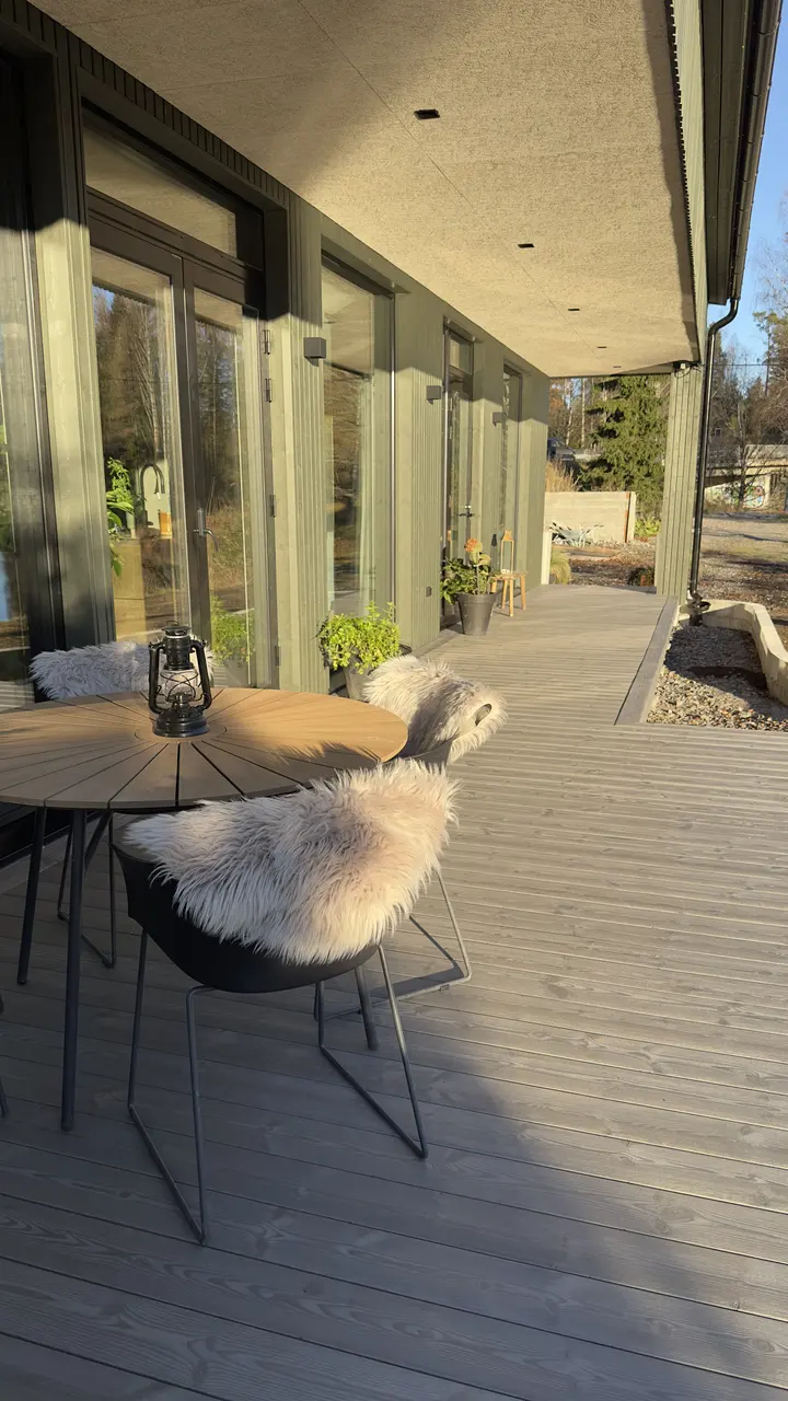 Pyöreä pöytä ja tuolit lampaantaljoineen katetulla terassilla.